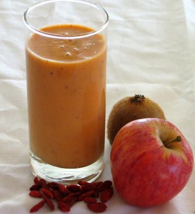 Copo com batido de iogurte e fruta, acompanhado de uma ma, um quivi e um punhado de bagas gojis